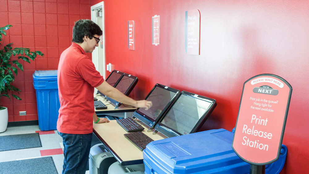 A student interacts with a print release station in the USU Computer Lab