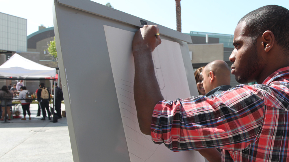 A student draws on an easel in the Plaza del Sol, USU at the Art 180 event